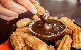 Hand dipping churro bite into chocolate sauce